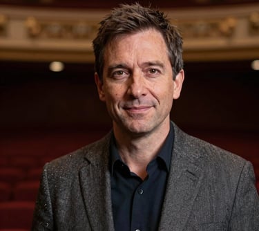 A professional headshot of a creative director in a sophisticated theater environment. The lighting is soft and flattering, emphasizing a mood of professional integrity and artistic passion. North American / Pacific Northwest US style attire.