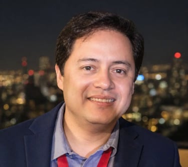 A dark hair guy with blue suit, smiling, named Albert Serrano, with a lighted city on his back