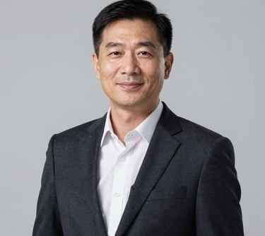 Professional corporate headshot of a business executive in a dark tailored blazer, smiling slightly. Minimalist light gray studio background, soft lighting, professional and highly trustworthy demeanor, Global / North American context.