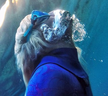 Woman snorkeling to the surface with goggles and air buccle on her face