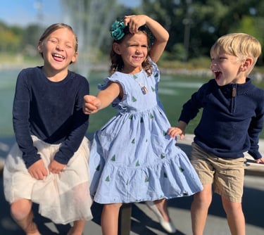 three children playing with a fountain in a park
