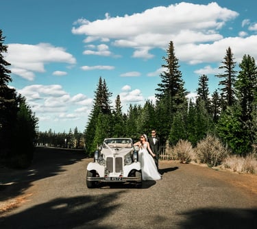 Bride and groom posing beside a vintage car on a scenic forest road, captured by Fred Art Studio.