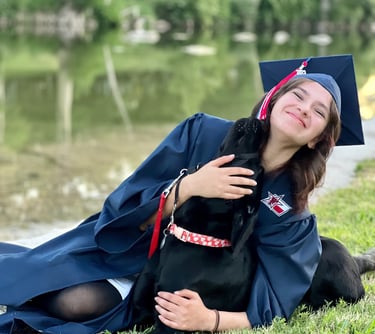 service dog in training nuzzles her puppy raiser who is wearing her cap and gown for senior pictures