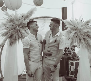 Smiling grooms celebrating a modern boho wedding ceremony under a pampas grass arch.