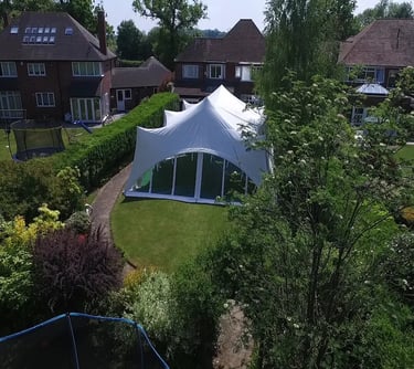 White garden party marquee tent set up in a lush residential backyard for an outdoor event.