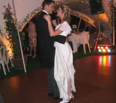 A bride and groom sharing their first wedding dance on a wooden floor inside a decorated tent.