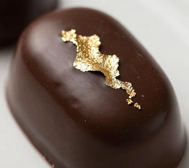Gourmet photography of a glossy dark chocolate entremet with gold leaf decoration, mirror glaze finish, high-end culinary magazine style, Western European / French.