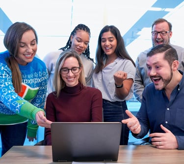 Diverse business team celebrating success while looking at a laptop screen in a bright office.
