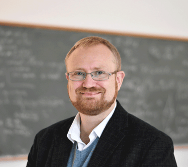 a man in a suit and glasses standing in front of a chalkboard