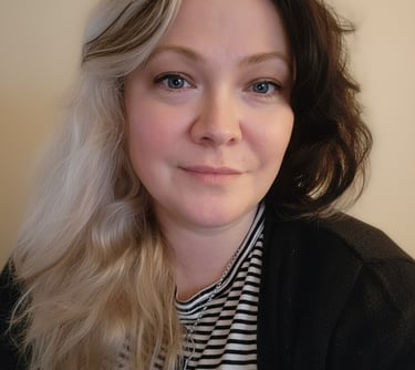 A woman with blue eyes and split-dye blonde and black hair wearing a striped shirt.
