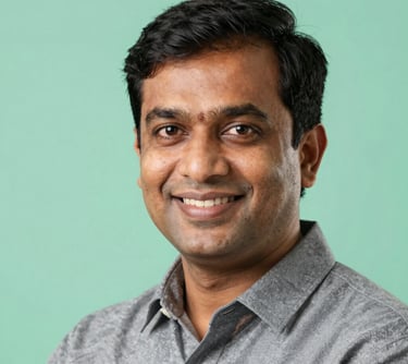 Professional headshot of a male Indian educator in his 30s, smiling, mint green background, professional studio lighting.