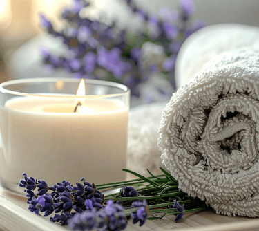 Scented candle with fresh lavender sprigs and a rolled white towel for a relaxing spa wellness experience.