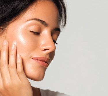 A woman applying moisturizing face cream to her glowing, hydrated skin for a skincare routine.