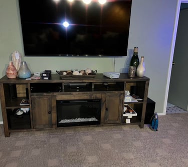 A rustic wooden TV stand with a built-in electric fireplace and decorative vases below a wall-mounted flat-screen TV.
