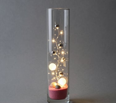 A sleek, modern vase with a smooth matte finish sitting on a wooden shelf against a soft neutral wall.