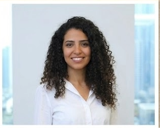 Smiling business professional woman with curly hair wearing a white shirt in an office.