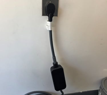Black electric vehicle charging cable plugged into a NEMA 14-50 wall outlet for home EV charging.