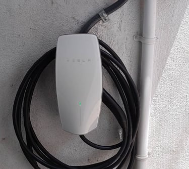 A white Tesla Wall Connector electric vehicle charger mounted on an exterior wall with a coiled black charging cable.