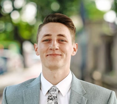 Portrait of Parker Oelrich, smiling slightly while wearing a light gray suit jacket, white shirt, an