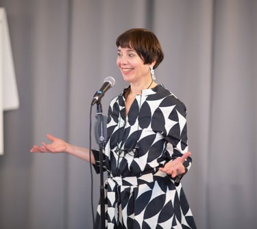 Female public speaking trainer, smiling behind microphone with confident body language. 