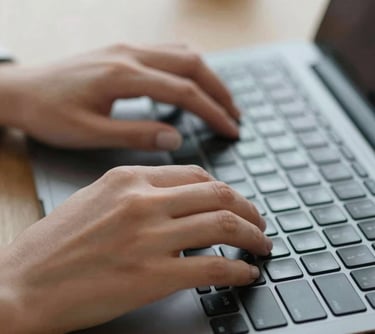 A detailed shot of a person's hands typing on a laptop keyboard in a bright office environment, symbolizing the creation of effective vacancy texts.