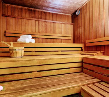 Traditional wooden cedar sauna room with tiered benches, bucket, ladle, and rolled white towels.