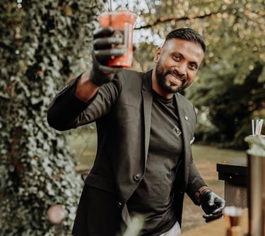 Professional mobile bartender in a black suit serving a fresh cocktail at an outdoor event.