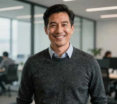 A portrait of a tech executive in a brightly lit North American workspace with glass walls. They are wearing a professional charcoal sweater and smiling warmly, projecting leadership and expertise.
