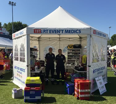 Event medical staff stand inside a white first aid tent equipped with emergency supplies at an outdoor festival.