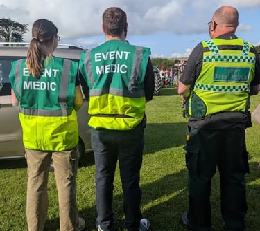 Three event medic first aid responders wearing high-visibility green vests standing in a field.