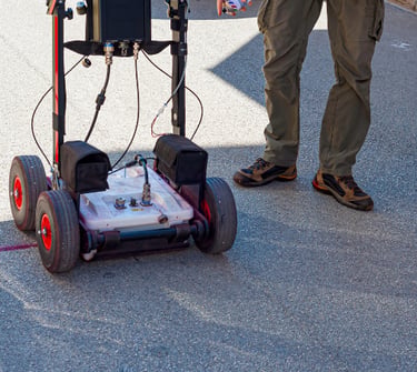 Technician using a ground penetrating radar system for utility mapping on an asphalt road.
