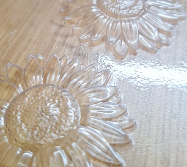 Clear plastic sunflower molds with textured petals and center seeds on a wooden surface.