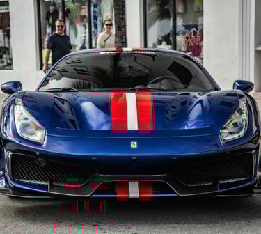 A blue Ferrari 488 Pista luxury supercar with red and white racing stripes parked on a city street.