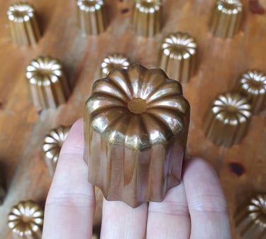 Un moule à cannelé en cuivre tenu dans une main