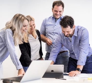 team pinelta standing around a table with a laptop