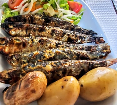 Five perfectly cooked Portuguese sardines served with salad and potatoes on a plate.