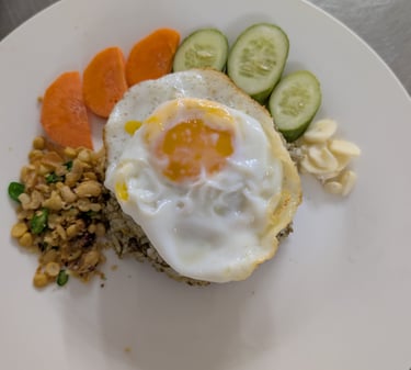 A plate of savory tearice topped with a sunny-side-up egg, served with sliced cucumbers and carrots.