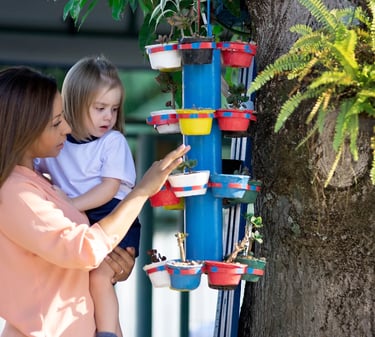 Teacher showing a toddler a vertical garden with colorful planters during an outdoor learning activi