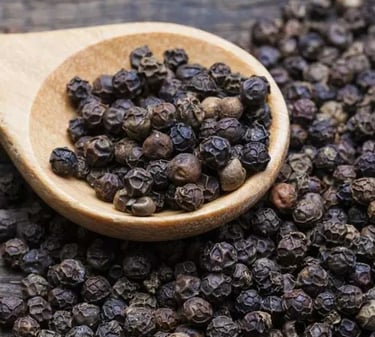 Organic whole black peppercorns in a wooden spoon on a rustic dark surface.
