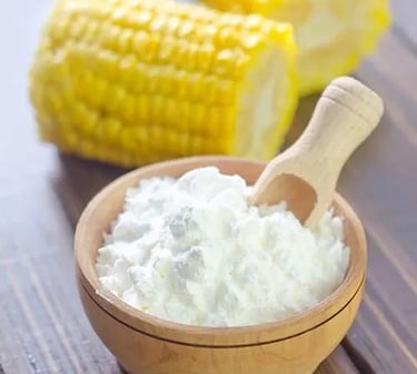 White organic cornstarch powder in a wooden bowl with a scoop next to fresh corn on the cob.