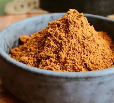 A small stone bowl filled with a heap of finely ground brown cumin spice powder on a wooden surface.