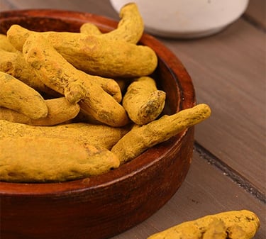 Whole dried organic turmeric roots piled in a dark wooden bowl on a rustic tabletop.