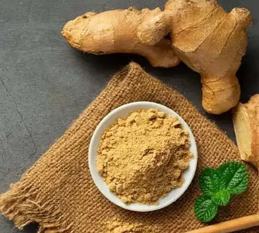 Fresh whole ginger root and organic ground ginger powder in a bowl on a rustic burlap cloth.