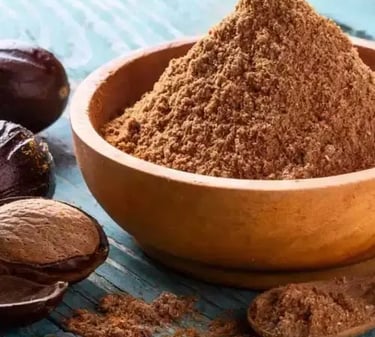 Ground nutmeg powder in a wooden bowl with whole nutmeg seeds on a rustic blue table.