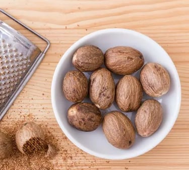 Whole nutmeg seeds in a white bowl next to a metal grater and freshly ground spice.