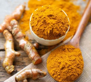 Organic turmeric powder in a bowl and spoon with fresh turmeric roots on a wooden table.
