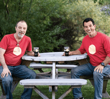 The Prairie Dog Tapproom owners, Jimmy and Michael Chidiac at a creekside table, toasting craft beer
