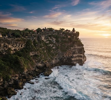 Dramatic limestone cliffs of Uluwatu at sunset, temple perched on the edge, golden-hour light hitting the ocean waves, 35mm lens.