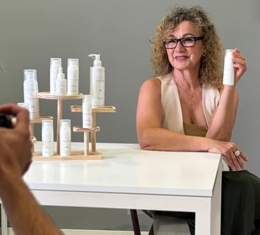 A woman posing with luxury skincare products for a professional photoshoot with a photographer.