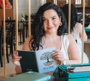 Raabe segurando caderno com livros e máquina de escrever ao lado.